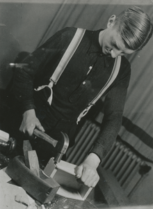 876578 Portret van een jongen, lid van een 'huisvlijtclub' van het St. Franciscus Liefdewerk, die een bakje aan het ...